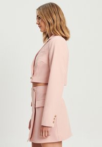 Kratka roza p blazer in krilo. Blazer ima zareznice, sprednje žepe in zlate gumbe; krilo je zamahnjeno. Gladka tekstura blaga.