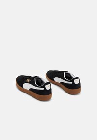 Sneakers en daim noir avec des accents blancs et des semelles en caoutchouc marron. Présente un logo doré sur le côté et une semelle intérieure texturée. Design basse.