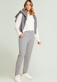 Lichtgrijze op maat gemaakte broek met subtiele witte polka dots, gecombineerd met een wit overhemd met knopen en een grijze trui over de schouders gedrapeerd.