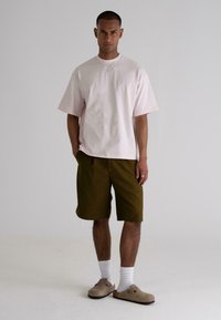 Light pink oversized t-shirt, dark green shorts, gray slip-on shoes, white socks. Minimalist design, relaxed fit, and simple tones.