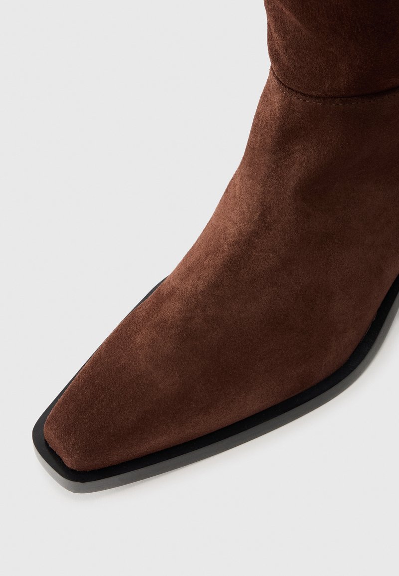 Brown suede ankle boot with a pointed toe and black rubber sole. The surface is soft with a smooth texture and minimal detailing.