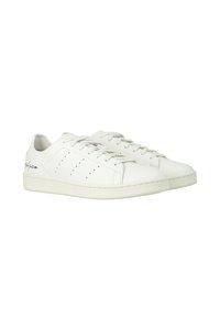 Sneakers bianchi in pelle con una texture liscia, lacci piatti, dettagli perforati sui lati e un branding sottile sul tallone.