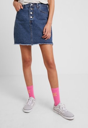 Gonna di jeans con orlo sfrangiato, chiusura frontale con cinque bottoni e due tasche. Abbinata a calzini rosa e sneakers grigie.