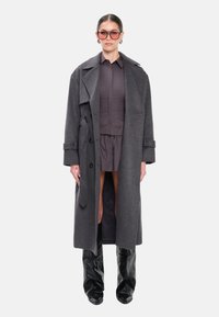 Lang grå uldfrakke med bælte i taljen, oversize revers, kombineret med et mørkt outfit og knælange, skinnende sorte støvler.