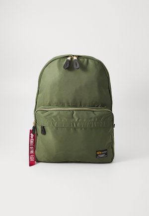 Mochila verde de nailon con cremalleras dobles, bolsillo frontal y etiqueta de tela. Presenta una textura suave y una forma redondeada con etiqueta de marca.