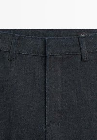 Dark denim trousers with a smooth texture, featuring a waistband and subtle stitching details. No visible pockets or hardware.