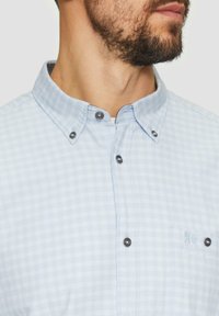 Hellblau kariertes Hemd mit Button-Down-Kragen, schwarzen Knöpfen und einer linken Brusttasche mit besticktem Detail. Aus 100 % Baumwolle.