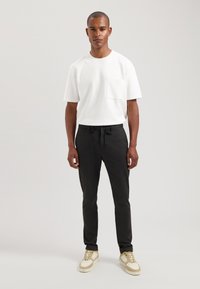 Witte t-shirt met korte mouwen en een borstzak, gecombineerd met zwarte joggerbroeken en crèmekleurige sneakers met een bicolor ontwerp.