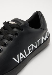 Fekete bőr sportcipő fehér "VALENTINO" felirattal, kerek orral, fűzős kivitelezéssel és texturált gumitalppal. Simább felület és megerősített fűzőlyukak.