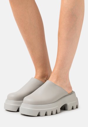 Gray slip-on clogs with a smooth leather finish, thick platform sole, and pronounced ridged texture; wide opening and rounded toe.