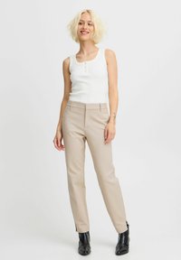 Débardeur côtelé blanc avec des accents de boutons associé à un pantalon beige ajusté. Bottines noires à la cheville complètent la tenue. Design minimaliste.