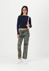 Jūrinės tamsiai mėlynos spalvos ilgos rankovės marškiniai, gėlių raštuoti šviesiai mėlyni džinsai, balti sportbačiai ir rožinė rankinė. Modelis dėvi rožinius akinius nuo saulės.