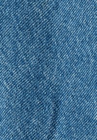 Tela de denim en un tono azul medio, con un clásico tejido de sarga. La textura parece suave con ligeras variaciones en el color.