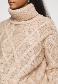 Beige Kabelstrick-Turtleneck-Pullover mit hohem Kragen, dicker Textur und komplizierten diagonalen Mustern, die Weichheit und Wärme betonen.