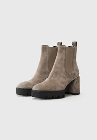Bottines en daim gris clair avec une semelle compensée noire épaisse et un talon bloc. Présente des panneaux élastiques sur les côtés et une languette à l'arrière.