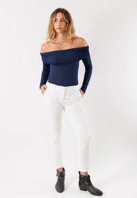 Body blu navy scollato spalle con maniche lunghe, abbinato a pantaloni bianchi attillati e stivaletti neri, creando un outfit a contrasto.