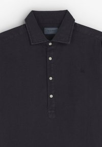 Chemise noire à manches longues avec col et cinq boutons blancs sur la patte de boutonnage avant, logo brodé sur la poitrine gauche.