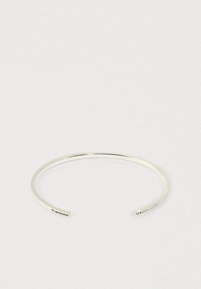 Tievs sudraba atvērta aproce ar izgravētu "le gramme" vienā galā un "7g 925" otrā pusē uz vienkārša baltā fona.