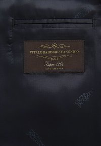 Ciemnoniebieska tkanina z brązową etykietą ze złotym napisem "Vitale Barberis Canonico 1663 Super 120's", wskazująca na wysoką jakość materiału.