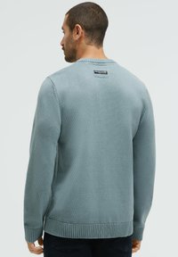 Hellblauer Strickpullover mit glatter Textur, gerippten Bündchen und Saum, versehen mit einem Logotag am hinteren Halsausschnitt.