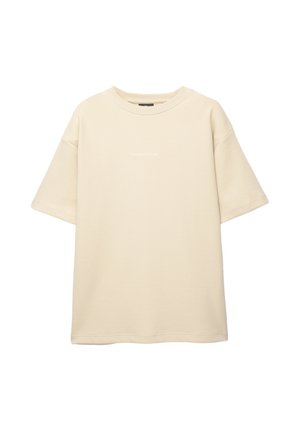 T-shirt en beige oversize à manches courtes fabriqué en tissu doux. Il possède un col rond et un petit texte sur le devant.