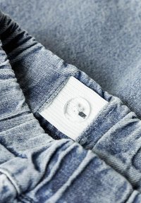 Črnilo blaga v bližnjem posnetku z nabranim pasom, svetlo modra barva, z belo etiketo in prozornim gumbom.