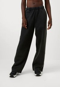 Μαύρες φαρδιές φόρμες με ελαστική μέση και μαλακή υφή. Το ύφασμα παρουσιάζει ελαφριές παραλλαγές, τονίζοντας την χαλαρή εφαρμογή.