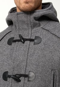 Cappotto in misto lana grigio con cappuccio, dotato di chiusure a moschettone e dettagli in pelle nera. Vista ravvicinata che mette in evidenza la trama e i dettagli.