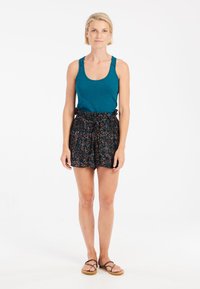 Teal tanktop met kantdetails, gecombineerd met zwarte shorts met bloemenpatroon en een elastische tailleband met strikjes. Bruine slippers.