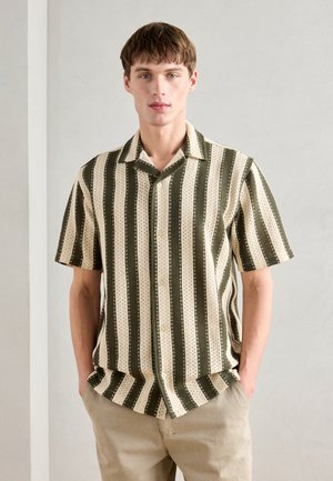 Chemise à manches courtes avec des rayures verticales vertes et crème, dotée d'une texture à motifs et d'une fermeture à boutons. Portée avec un pantalon beige.