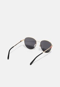 Gold metal frame sunglasses with round dark lenses, black temple arms, and a small red accent on the earpiece. Lightweight design.