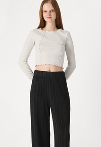 Haut court à manches longues en ribbed gris clair avec un ourlet festonné, associé à un pantalon large plissé noir. Texture lisse tout au long.