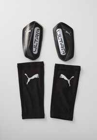 Zwarte voetbalscheenbeschermers met het label "ULTRA Flex" en metalen accenten, gecombineerd met zwarte stoffen mouwen die voorzien zijn van een wit Puma-logo.