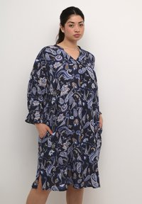 Vestido azul marino con un patrón de paisley, escote en V, mangas largas con puños acampanados y bolsillos laterales. Tejido suave con un corte holgado.