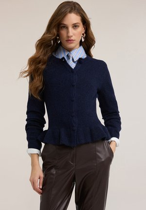 Granatowy kardigan z wełny z peplum, dekoltem w serek i zapięciem na guziki. Stylizowany na jasnoniebieską koszulę w paski. Gładka faktura z długimi rękawami.