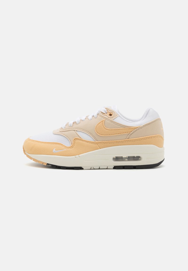Sapatilha Nike Air Max 1 em branco e pêssego claro, com materiais de malha e camurça, biqueira redonda, atacadores brancos e uma unidade de ar visível na sola.