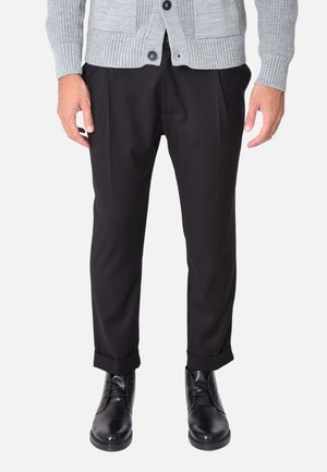 Pantaloni neri su misura con una piega sul davanti, con orli a maniche, abbinati a scarpe nere lucide e a un cardigan a maglia grigio chiaro.