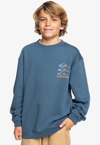Sudadera azul con cuello redondo, corte holgado y mangas largas. Presenta estampados gráficos en el lado izquierdo del pecho y está hecha de una suave mezcla de algodón.