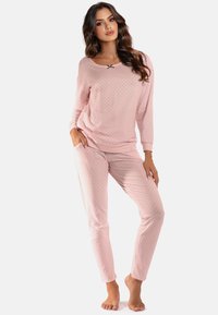 Helles rosa Pyjama-Set aus weichem Stoff; mit langen Ärmeln, Punkten, seitlichen Taschen und einem schwarzen Schleifenakzent am Ausschnitt.