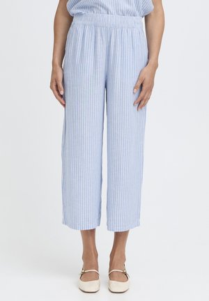 Femme portant un pantalon ample à rayures verticales bleu clair et blanc avec une taille élastique, et des ballerines crème avec des lanières.