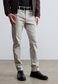 Svetlosivé bavlnené nohavice so širokým strihom, nosené s čiernym opaskom a čiernymi topánkami. Hladká textúra bez viditeľných vzorov.