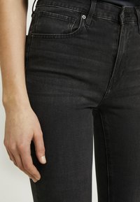 Jeans de mezclilla negra con un corte ajustado, que presentan un diseño clásico de cinco bolsillos, detalles de costura sutil y herrajes metálicos.