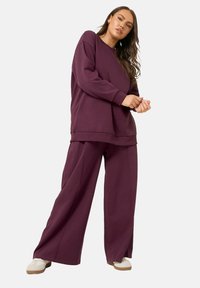 Lila oversized sweatshirt och matchande vidbyxor i mjukt tyg, med en avslappnad passform och minimala sömdetaljer.