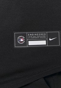 Tessuto atletico nero con un motivo testurizzato presenta un'etichetta con la scritta "Merce Autentica" e "Progettato secondo specifiche esatte" con il logo Nike.