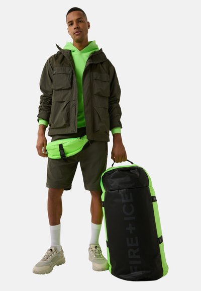 Black and neon green backpack, cylindrical shape, textured fabric, featuring the logo "FIRE + ICE" on the front, carried by a model in sporty attire.