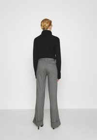 Suéter negro de cuello alto acanalado combinado con pantalones de pierna ancha grises que cuentan con dobladillo vuelto y sutiles bolsillos traseros.