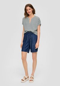 Gestreepte top met korte mouwen en een sleutelgat halslijn, gecombineerd met losse denim shorts en stevige beige sandalen. Casual outfit in gedempte tinten.