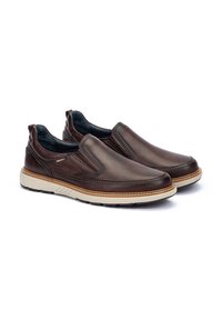 Zapatos marrones de piel de tipo slip-on con parte superior texturizada, suela de goma beige en contraste y paneles elásticos laterales para una fácil entrada.