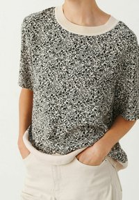 Korte mouw top van lichte stof met een zwart en crèmekleurig bloempattern, met een geribbelde crèmekleurige halslijn en een relaxte pasvorm.