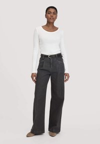 Witte blouse met lange mouwen, gecombineerd met high-waisted, wijde, donkergrijze jeans, afgewerkt met een zwarte riem. Zachte textuur, minimalistisch ontwerp.